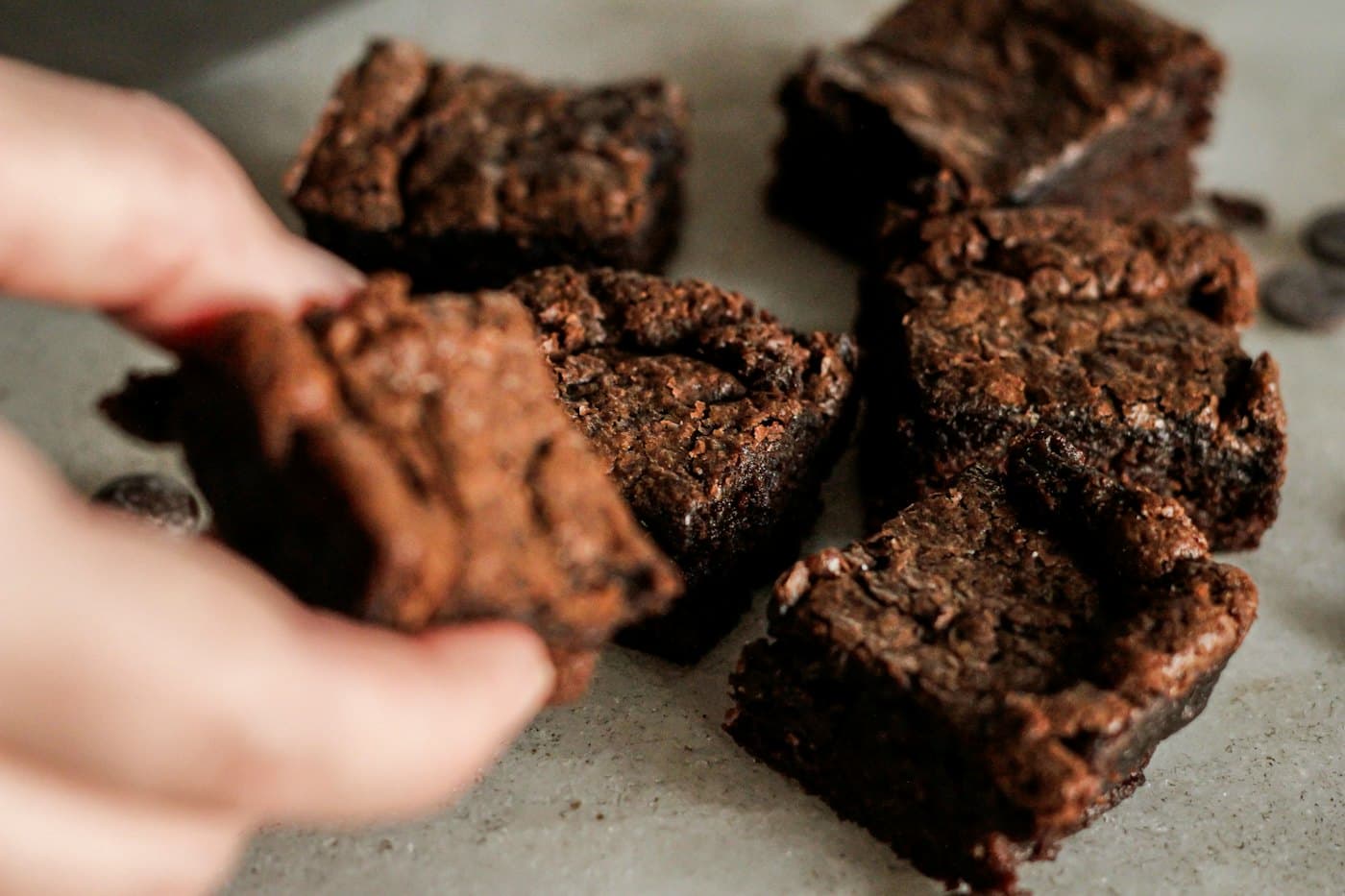 A hand picking up a brownie from the pile