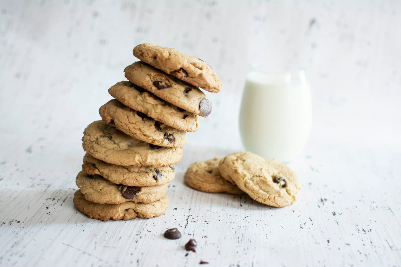 A stack of chocolate chip cookies beside a glass of milk