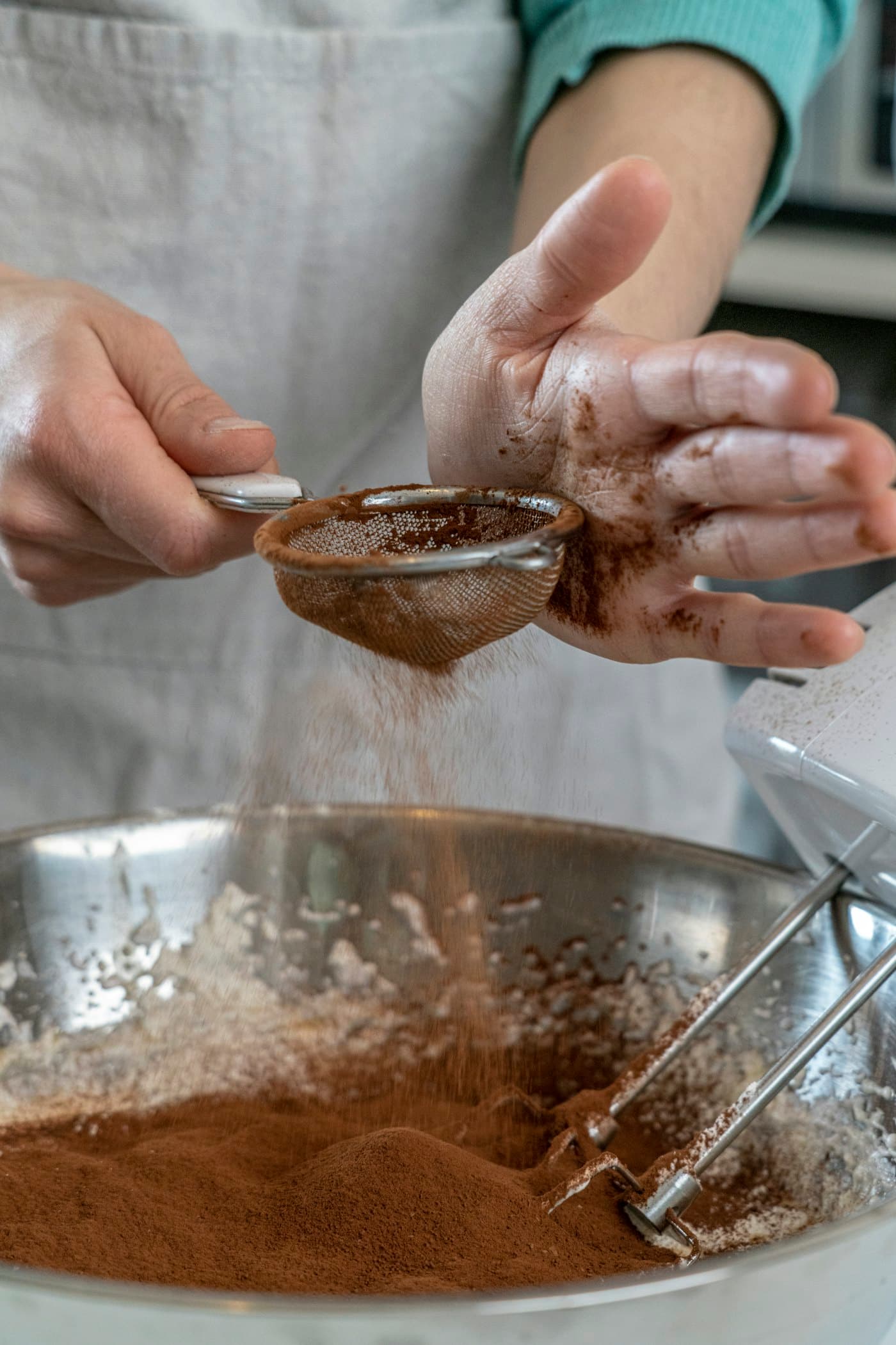 Hands sifting cocoa into a mixing bowl